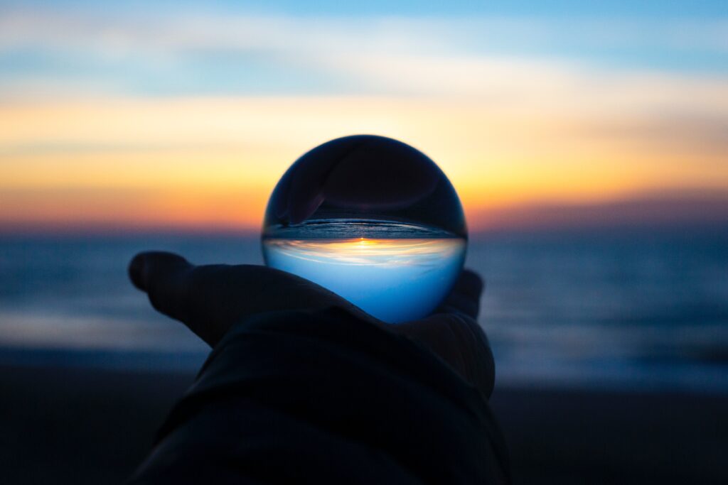 person holding clear ball looking at the sunrise reflection